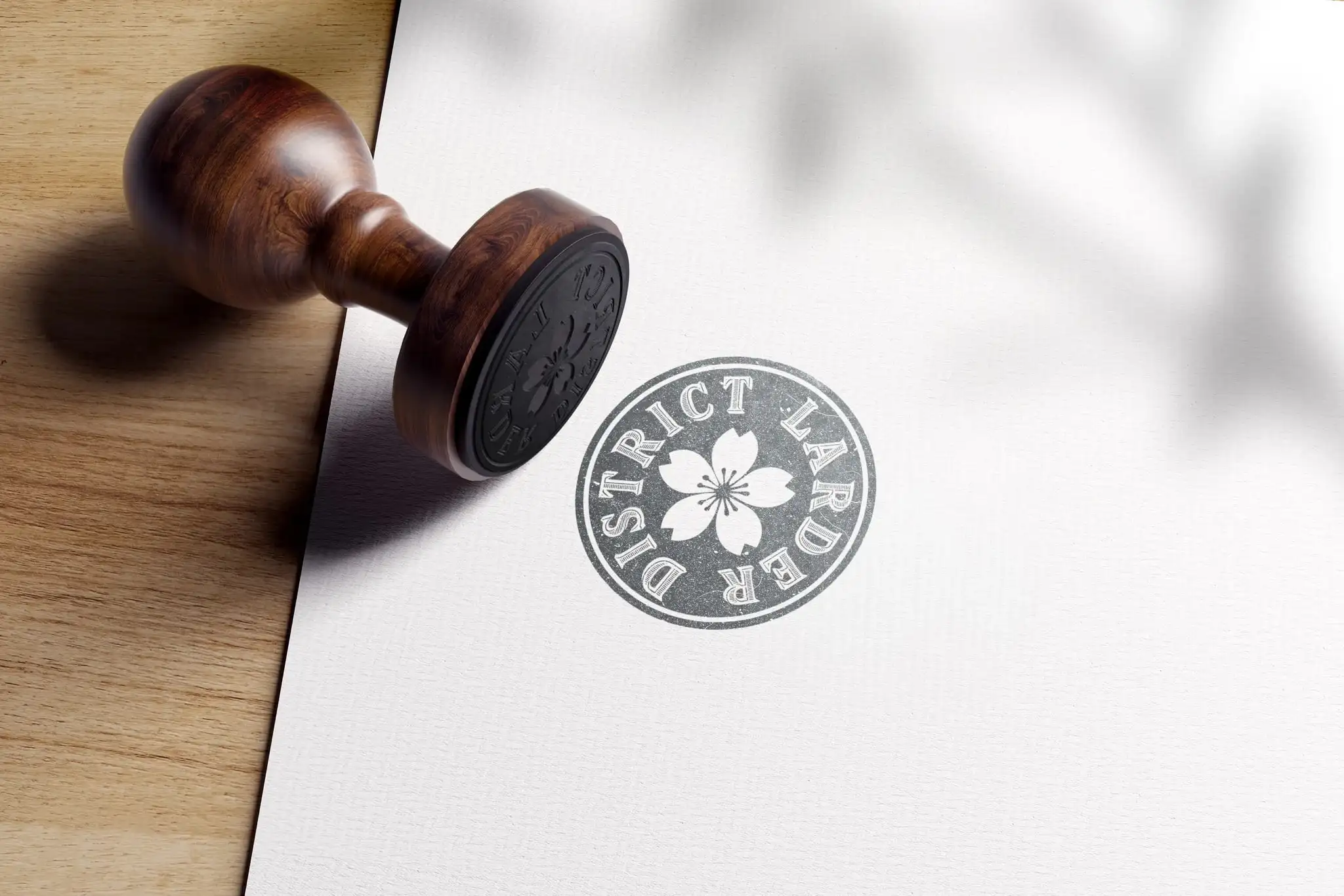 A wooden stamp beside the round District Larder cherry-blossom seal printed on white paper