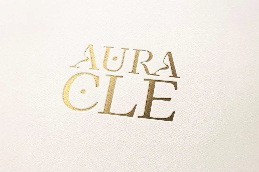 The stacked Auracle logo in gold foil, pressed into textured cream paper