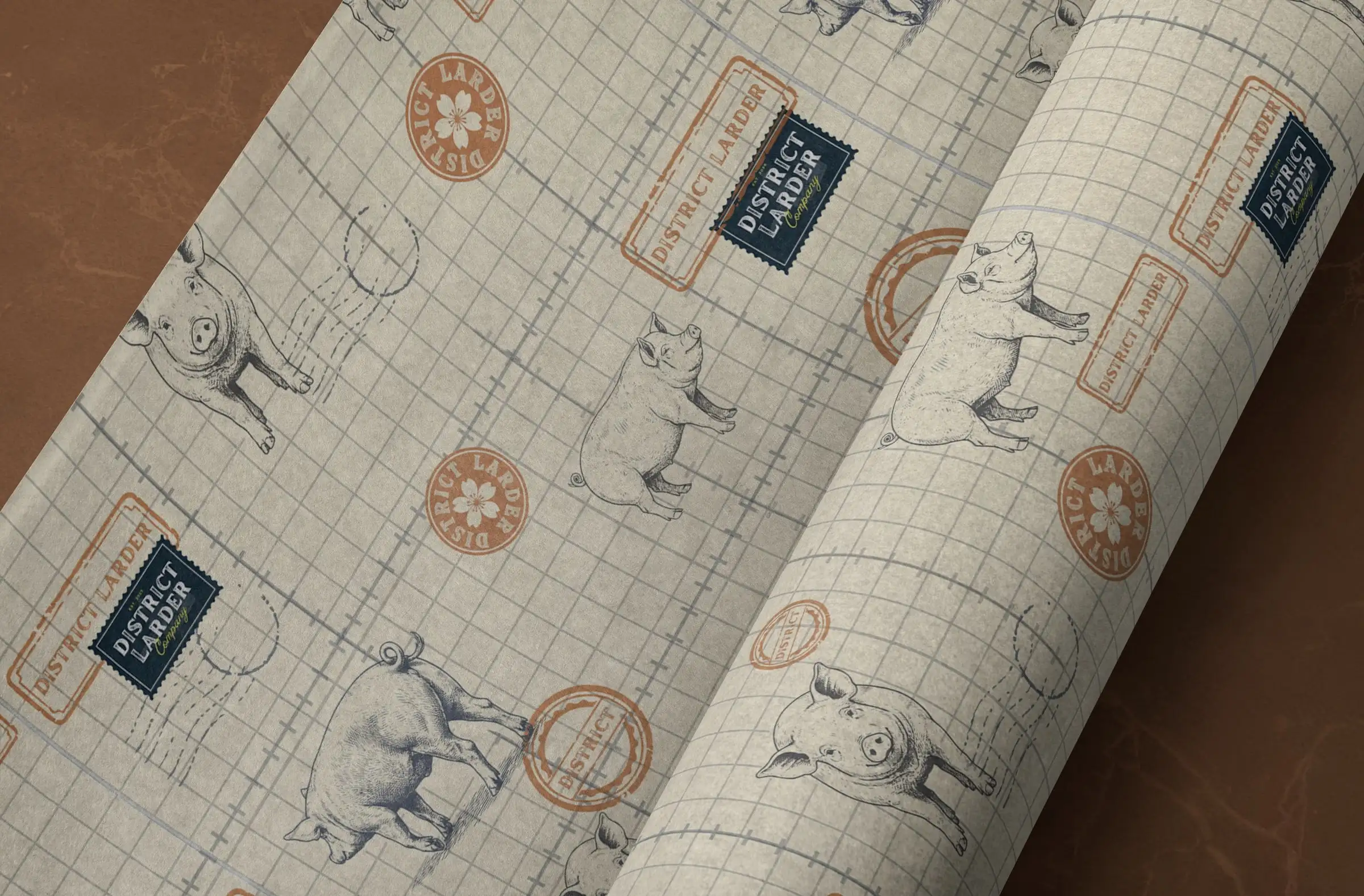 A roll of District Larder grid paper printed with pig illustrations and orange and navy stamps